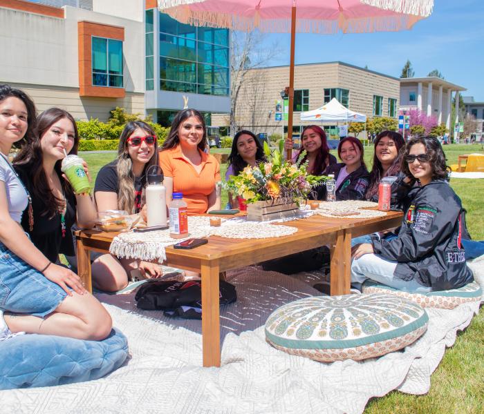 Group of people picnicking on a lawn and smiling at the camera