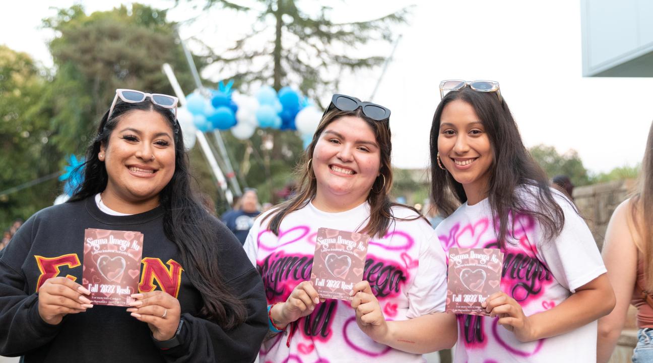three students holding up a sign for their sorority