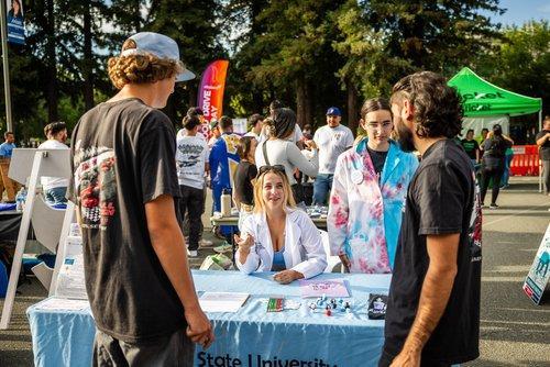 students speaking with peers across a table at an outdoor resource fair event