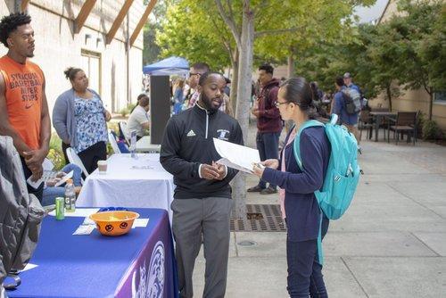 two students speaking together at an table outdoors