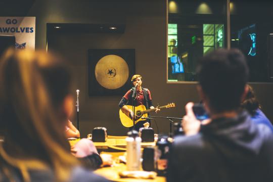 Man standing on stage with guitar with an audience 